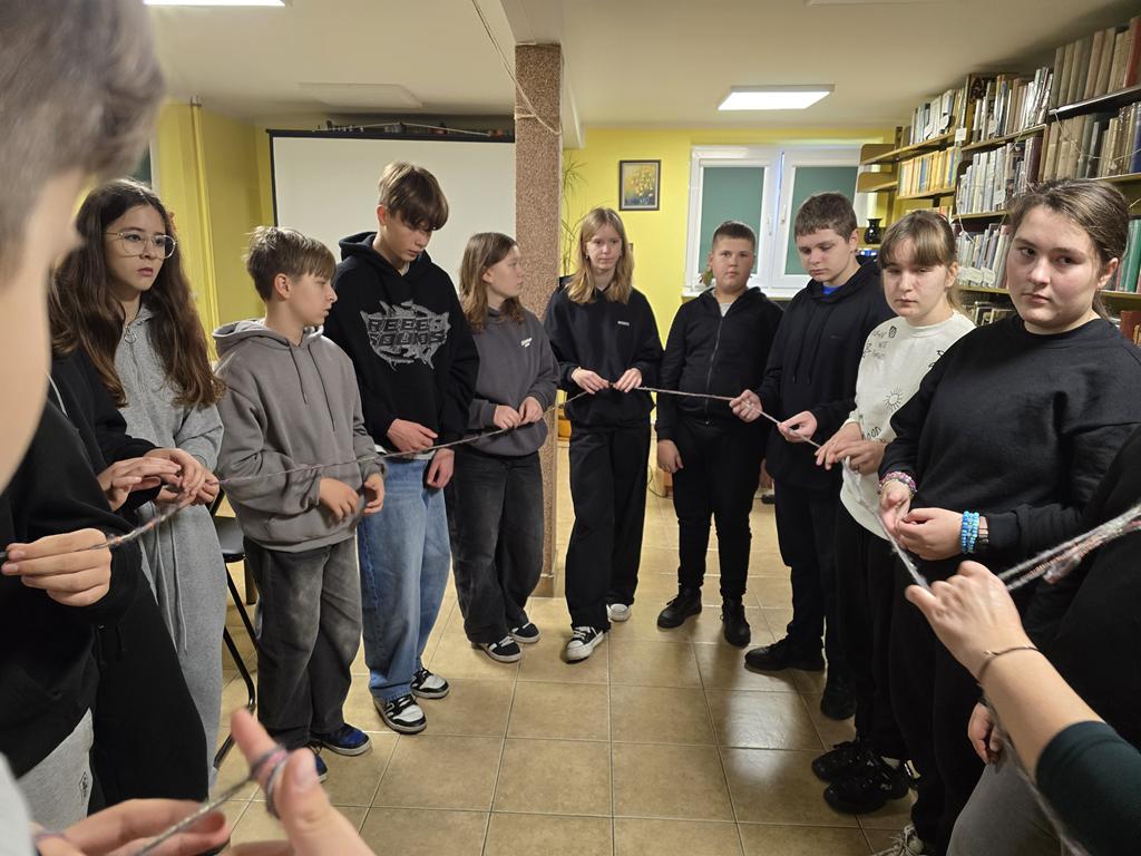 Dzieci stoją w kręgu na środku Sali, trzymają w ręku nić z rozwiniętego kłębka kolorowej włóczki.