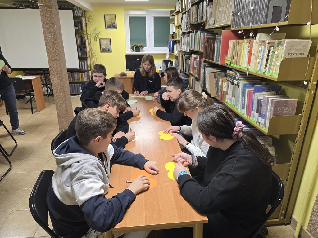 Dziewięcioro dzieci siedzi przy stoliku i pisze na kolorowych papierowych sercach.