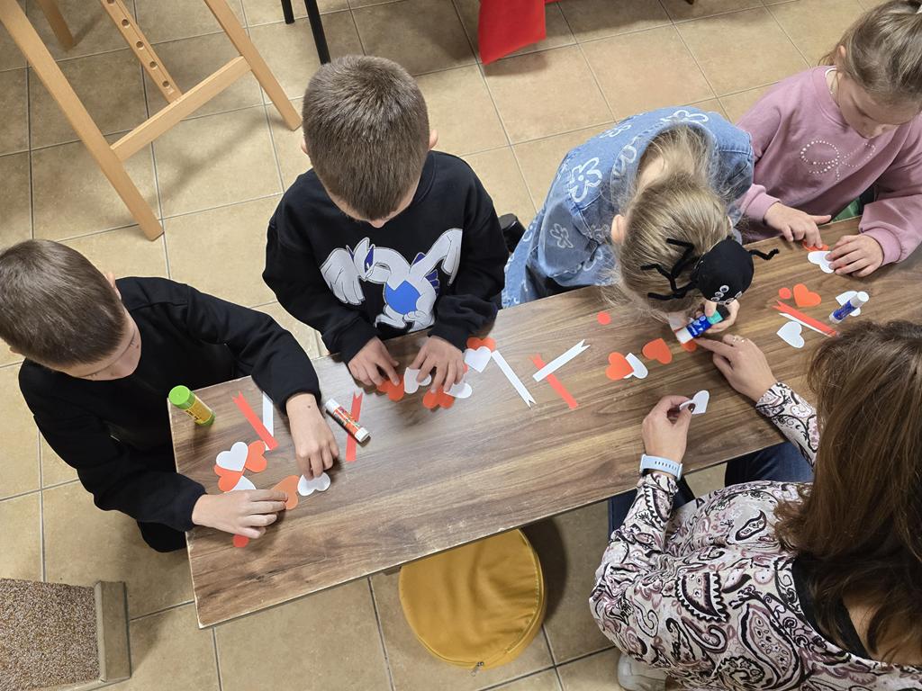 Pięcioro dzieci w kolorowych ubrania siedzi przy ławce, wykonują kotylion.