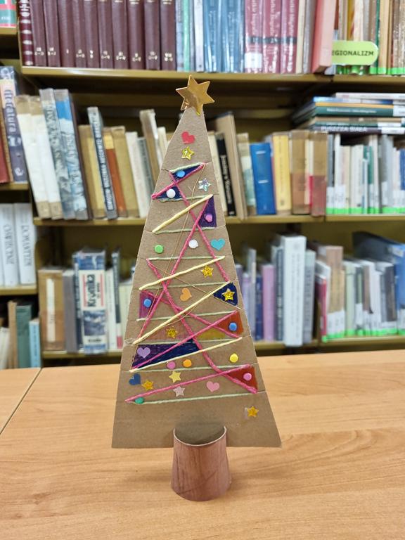 Jedna choinka wykonana z kolorowego papieru i tektury. W tle regały z książkami.